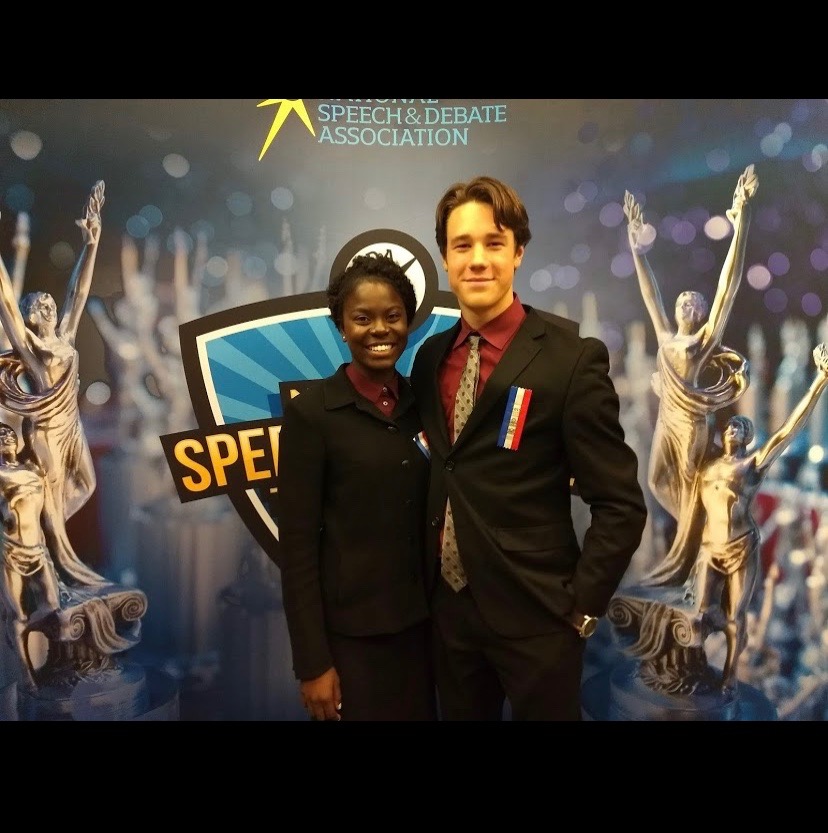 Sandra Leybold (12) and her partner Alex Nydahl (12) pose in front of the National Speech and Debate Association backdrop at the Nationals Tournament in Dallas, Texas. 