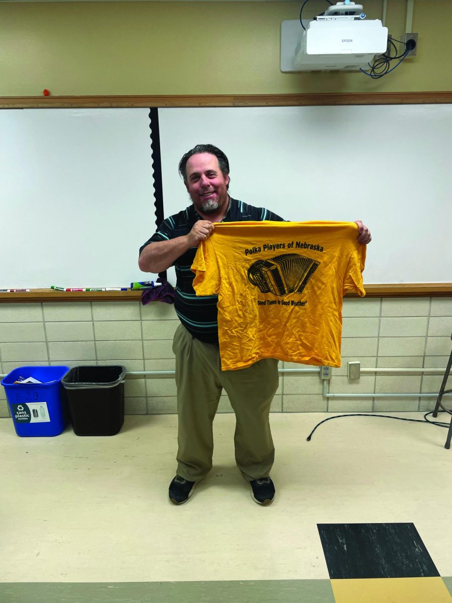 Lincoln Southeast English teacher Chris DeAmbrose poses with a t-shirt that reads “Polka Players of Nebraska. Good times in Good Weather.” 
Photo Credit: Kyah Martinez